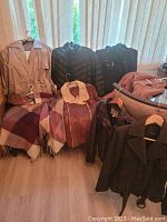 Group photo showing multiple women's jackets of different styles including trench coat, puffer jacket, shearling leather coat, and fleece jacket on hangers and folded on chair.