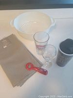 Photo of all lot items together on white surface including strainer, glasses, bottle opener, tea towel, and travel mug