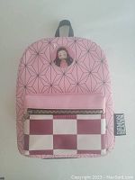 Front view of mini backpack showing pink geometric pattern, badge with anime character, and front zippered pocket with checkered design.