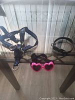 Photo showing the three small dog accessories including a black collar and pink heart-shaped sunglasses, alongside the harnesses