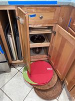 Open kitchen cabinet with various baking sheets, trays, cutting boards, and cooking racks stacked inside and around the cabinet space.