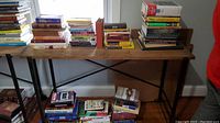 Wide view of three stacks of mixed paperback and hardcover books on folding table