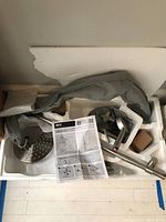 Photo of KES faucet and shower head kit components in foam packaging including shower head, shower arm, faucet body, and instruction manual.