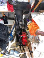 Vertical black steel log splitter frame leaning against wall surrounded by items