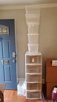 Full view of multiple stacked clear plastic storage totes and tall drawer unit near a door