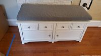 Front and top view of the white storage bench with gray cushion showing three small drawers and cabinet doors below.