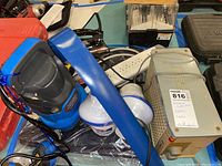 Photo showing the blue and black portable submersible sump pump with its power cord, power strip, chlorine tablet container, and other items on the table.