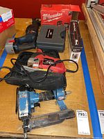 Overview of all tools on surface showing pneumatic stapler, Skil orbital saw, Milwaukee tool in box, Bosch nailer box, and cordless wrench