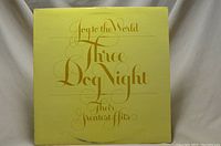 Front cover of the vinyl album showing the title 'Joy to the World Three Dog Night Their Greatest Hits' in gold script on a yellow background.