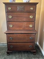 Front view of antique wooden dresser showing five drawers, ornate hardware and carved detailing on top drawer.