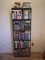 Full view of a black bookcase stuffed with various books arranged on multiple shelves and some stacked on top.