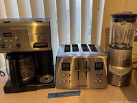 Three Cuisinart stainless steel kitchen appliances on countertop including coffee maker, toaster, and blender.