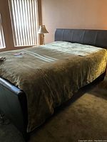Forest green heated blanket spread over king-sized bed with bedside lamp near window.