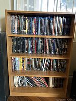 Wooden shelf filled with DVDs arranged on four shelves including a diverse movie collection.
