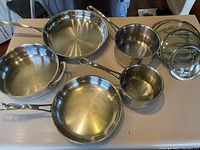 Set of five stainless steel pots and pans with two matching glass lids seen on kitchen counter