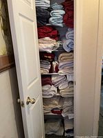 Full view of lined closet showing shelves stacked with folded linens including sheets, towels, blankets in various colors and fabrics.