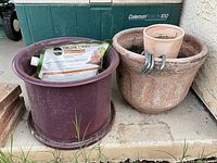 Two large plastic pots on outdoor concrete slab with gardening products inside one