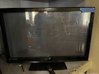Photo of Vizio flat screen TV on stand, black frame, reflecting room interior.