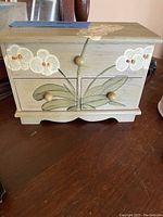 Closed wooden jewelry box with white orchid painted on front, three fingers knobs, decorative scalloped bottom edge.