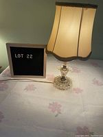 Boudoir lamp lit on a table with fabric shade and textured clear glass base, along with Lot 22 sign