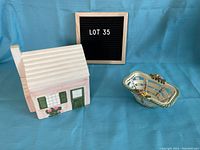 Photo showing the ceramic cookie jar shaped like a house and the small hand-painted basket beside it from a frontal angle.