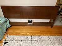 Full view of headboard against a wooden floor and wall, showing entire piece with bottom rail and leg supports.
