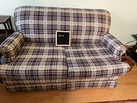 Front view of vintage two-seater loveseat showing plaid upholstery and rounded arms.