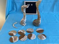 Two onyx marble sculptures (swan and dog) with detached tail piece and six octagonal coasters on blue background