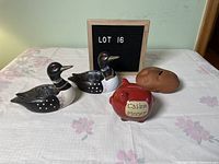 Four piggy banks on a floral tablecloth including two loon-shaped banks, one red pig bank labeled 'Casino Money', and one potato-shaped bank.