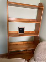 Full view of pine shelf showing four shelves and open back against wall, near armchair.
