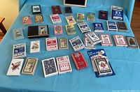 Overview of 39 assorted decks of playing cards spread on blue sheet, showing variety of brands and conditions