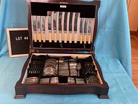Photo of complete silver plate and stainless steel cutlery set displayed inside an open wooden case showing organized compartments and utensils.