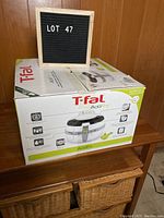 Closed original box showing T-fal ActiFry branding and product info, placed on wooden furniture