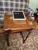 Full view of wooden telephone table with worn finish on tabletop, placed in front of patterned couch and rug.