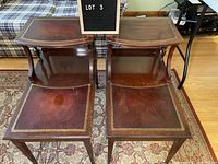 Pair of vintage reddish brown wooden side coffee tables with lower shelves and gold decorative borders on tops, showing surface wear.