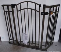 Full view of adjustable metal dog gate, showing three connected panels and manual attached to center panel.