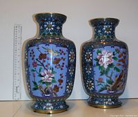 Two matching blue Asian vases placed side by side with a ruler next to them for scale, showing floral and bird motifs on the vases