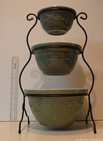 Set of three sage green Longaberger pottery nesting bowls displayed in black wrought iron three-tier stand with ruler for scale.