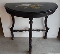 Front view of the black half moon wooden side table showing the curved shape, three ornate turned wooden legs, and stretcher support.