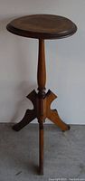 Front view of the wooden plant stand showing its round top, central turned column, and tripod base.