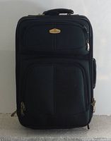 Closed view of large black Ricardo suitcase showing front zippered compartments and top handle