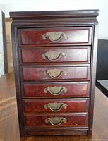 Frontal view of the jewelry box showing all five drawers with brass handles and the wooden textured finish.