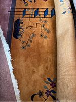 Partial view of rug rolled to show rust background, geometric motifs and ivory fringe