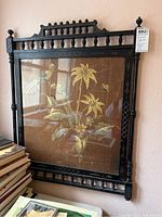 Full view of black Eastlake style walnut frame with spindle details and the needlework featuring birds, flowers, and leaves inside the glass-covered frame.