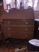 Full view of the slant front desk closed, showing three drawers with brass oval handles and slant front panel.