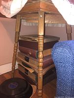 View showing the square top, turned legs with decorative rings, lower shelf with stored items underneath stand.