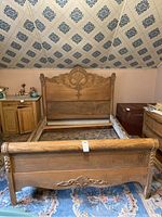 Full view of the antique oak sleigh bed headboard and footboard with blue patterned carpet and light pink walls in the background.