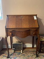 Front view of serpentine front walnut ladies desk with drop lid and single drawer, with 1320 watt space heater underneath.