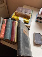 Front view of a collection of antique books, including leather-bound journal and cookbooks, showing worn spines and colorful vintage covers