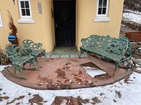 Wide view of entire cast iron seating set on front porch with snow-covered ground.